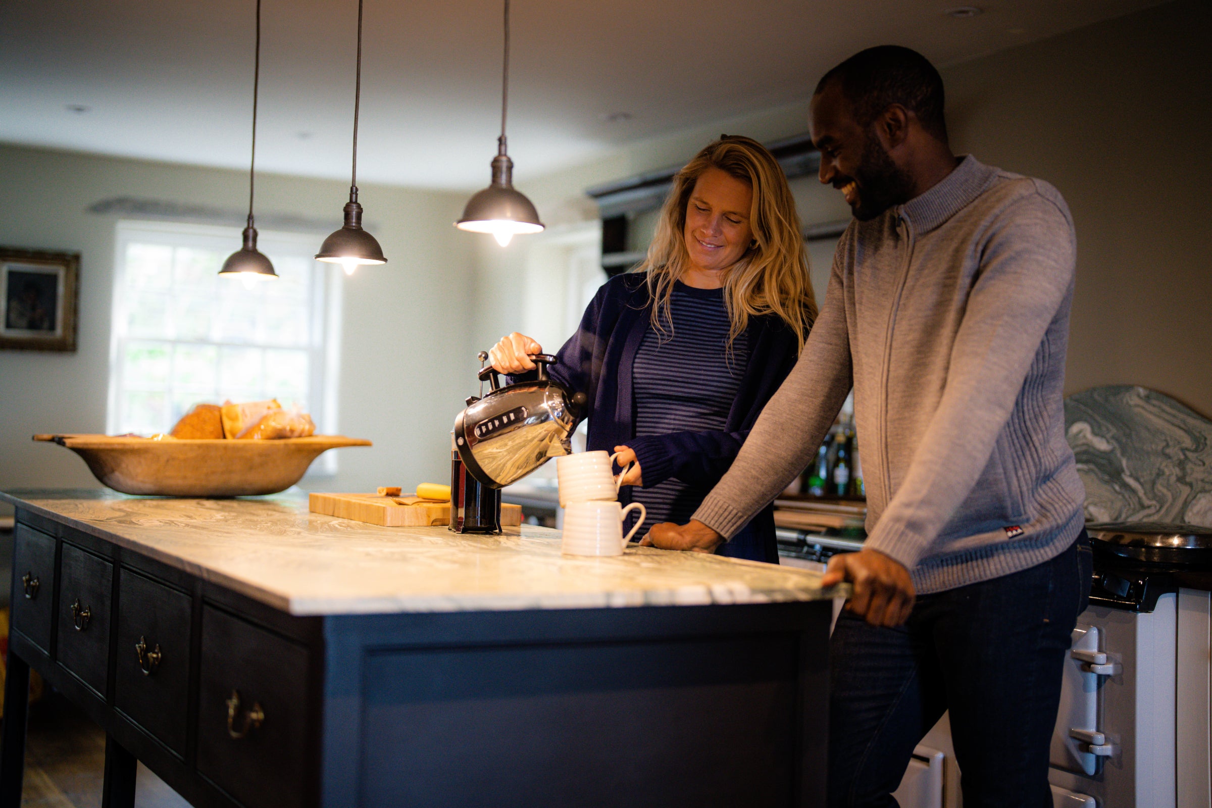 A man and a woman in a cosy kitchen, sharing a moment as the woman pours tea