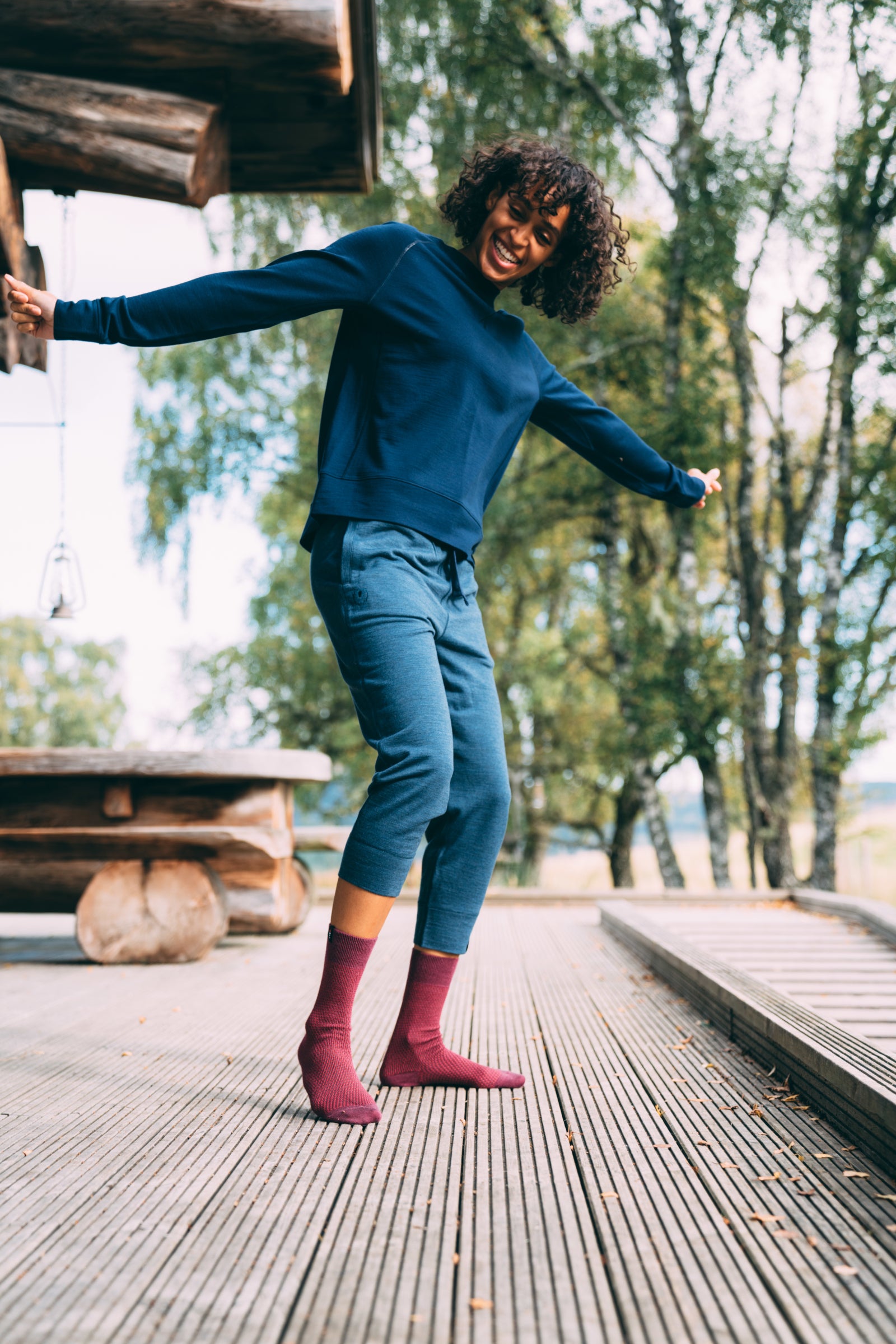 A woman outdoors, smiling and dancing on a wooden deck